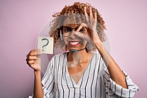 African american call center agent woman using headset holding paper with question mark with happy face smiling doing ok sign with