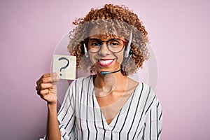African american call center agent woman using headset holding paper with question mark with a happy face standing and smiling