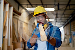 African American carpenter man hold timber or wood stick also look forward to check quality of wood product in factory workplace