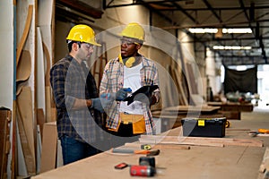 African American and Caucasian carpenter man discuss together about wood work using tablet in factory workplace