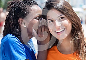 African american and caucasian girlfriend whispering in the city