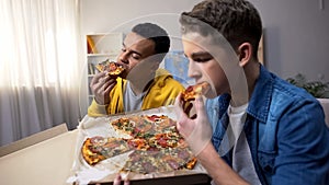 African-american and caucasian teenage friends enjoying pizza, unhealthy food