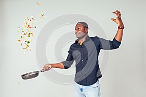 African American chef holding a frying pan wizard man is cooking magic flying food salad, carrot, garlic, onion, pepper