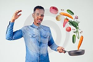 African american chef kitchener holding a frying pan wizard man cooking magic flying food salad, carrot, garlic, onion