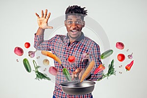 African american chef kitchener holding a frying pan wizard man cooking magic flying food salad, carrot, garlic, onion