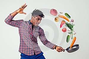 African american chef kitchener holding a frying pan wizard man cooking magic flying food salad, carrot, garlic, onion