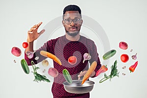 African american chef kitchener holding a frying pan wizard man cooking magic flying food salad, carrot, garlic, onion