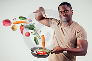 African american chef kitchener holding a frying pan wizard man cooking magic flying food salad, carrot, garlic, onion