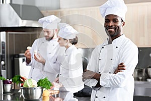 African american chef standing with folded arms in front of his colleagues
