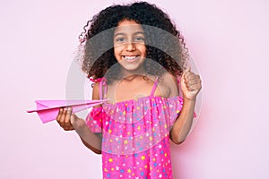 African american child with curly hair holding paper airplane screaming proud, celebrating victory and success very excited with