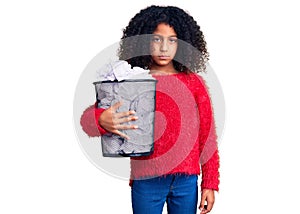 African american child with curly hair holding paper bin full of crumpled papers thinking attitude and sober expression looking