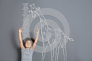 African-American child measuring height near chalk giraffe drawing on grey