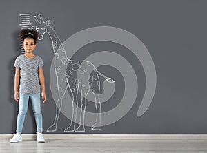 African-American child measuring height near chalk giraffe drawing on grey wall