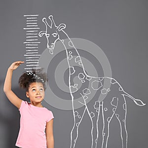 African-American child measuring height near chalk giraffe drawing