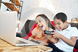 African American children - a boy and a girl holding a gamepad in their hands, play computer games on a laptop and laugh