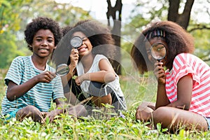African American children sitting in the grass and looking through the magnifying glass between learn beyond the classroom. .