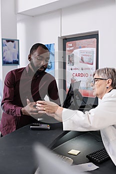 African american client standing at pharmacy counter discussing medication treatment with senior pharmacist