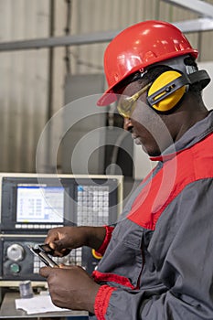 African American CNC Machine Operator In Personal Protective Equipment Checking Measurements With Digital Vernier Caliper