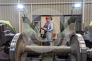 African American CNC Machine Operator Talking To Caucasian Production Manager Next To Lathe Machine - Train Wheel Manufacturing