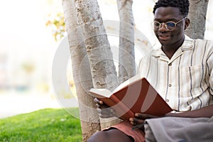 African american college student reading book on campus. Young black man reading book outdoors. Copy space.