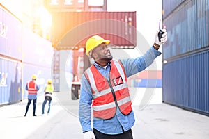 African American container operators wearing yellow helmets and safety vests control via walkie-talkie workers in container yards