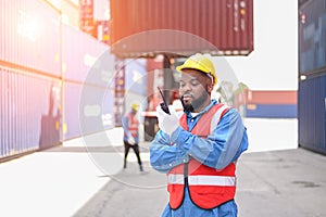 African American container operators wearing yellow helmets and safety vests control via walkie-talkie workers in container yards