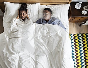 African American couple on bed, man snoring and disrupting woman photo