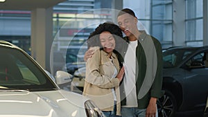 African American couple buyers customers happy owners joyful smiling woman man cuddling choosing modern car at vehicle