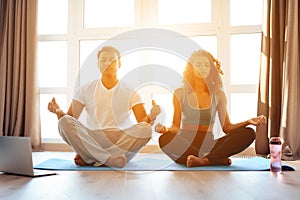 African American couple doing yoga exercises at home. They sit on the floor on yoga mats in a lotus position.