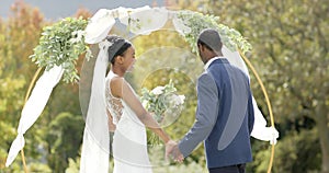 African american couple holding hands and smiling at their wedding in sunny garden, in slow motion