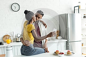 african american couple kissing and taking selfie with smartphone