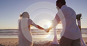 African american couple in love getting married, holding hands on the beach at sunset