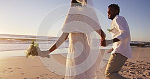 African american couple in love getting married, holding hands on the beach at sunset