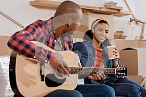 african american couple playing on acoustic guitar in new home