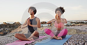 African american couple practicing yoga and meditating together on the rocks near the sea