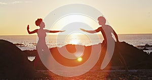 African american couple practicing yoga together on the rocks near the sea during sunset