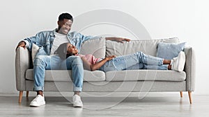 African american couple spending weekend together lying on couch