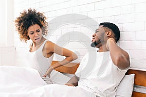 African-american couple suffering from back and neck ache in bed