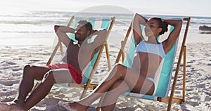 African american couple sunbathing while sitting on deck chairs at the beach