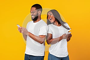 African american couple using cellphones, yellow studio wall