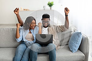 African american couple using laptop, celebrating win