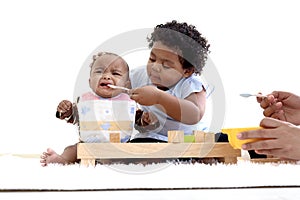 African American curly hair girl trying to feed her little sister with spoon of food, infant eating healthy homemade baby food,