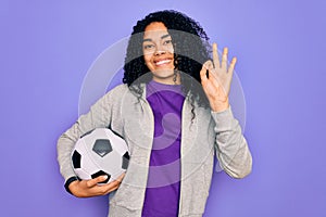 African american curly player woman playing soccer holding football bal over purple background doing ok sign with fingers,