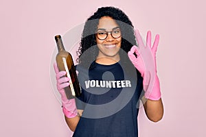 African american curly woman wearing volunteer t-shirt doing volunteering recycling glass bottle doing ok sign with fingers,
