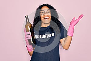African american curly woman wearing volunteer t-shirt doing volunteering recycling glass bottle very happy and excited, winner