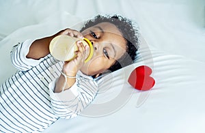 African american cute baby boy drinking milk from bottle and sleeping on bed with a red heart at home, Children need love