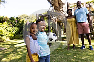 African american cute siblings with soccer ball and grandparents standing in park