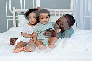 African-American dad plays with kids babies at home on the bed in the bedroom and cuddle, father`s love