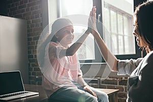 African american daugher giving high five to her mother while sitting on table