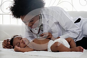 African american doctor examining black baby boy sleeping on bed with stethoscope